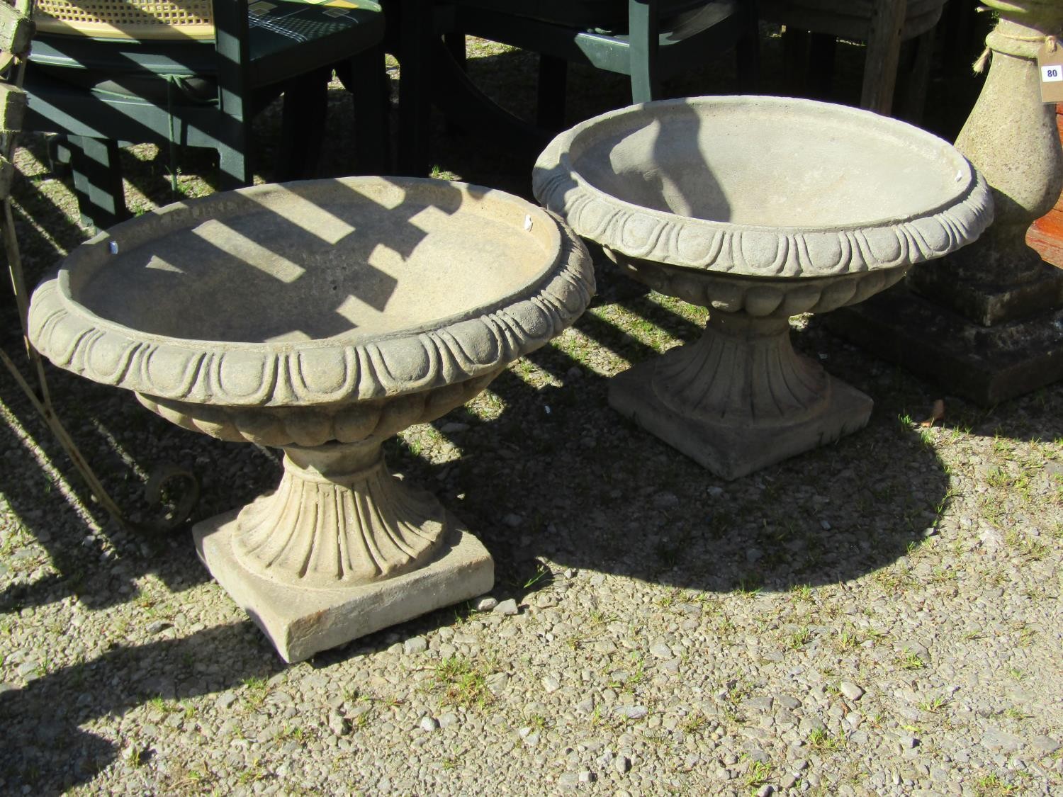A pair of cast composition stone garden urns, the squat circular lobbed bowls with egg and dart