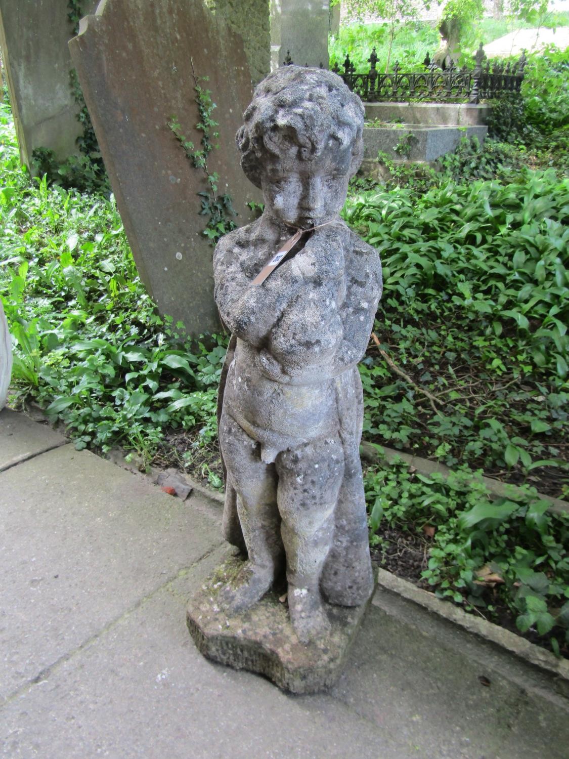 A weathered cast composition stone garden ornament in the form of a boy wearing a long trench coat