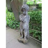 A weathered cast composition stone garden ornament in the form of a boy wearing a long trench coat