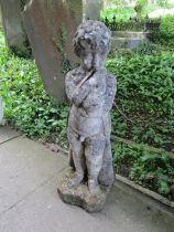 A weathered cast composition stone garden ornament in the form of a boy wearing a long trench coat