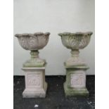 A pair of cast composition stone garden urns with circular acanthus leaf bowls raised on loose