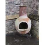 A large weathered clay chimenea raised on a simple steel stand, 107 cm high