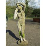 A weathered cast composition stone garden ornament in the form of a standing classical female nude