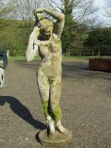 A weathered cast composition stone garden ornament in the form of a standing classical female nude