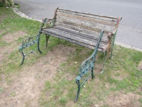 A weathered two seat garden bench with slatted seat raised on decorative pierced cast iron end
