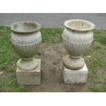 A pair of small weathered cast composition stone urns with reeded bowls and flared rims, raised on