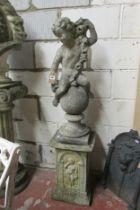 A weathered cast composition stone cherub astride a sphere clutching a floral garland raised on a