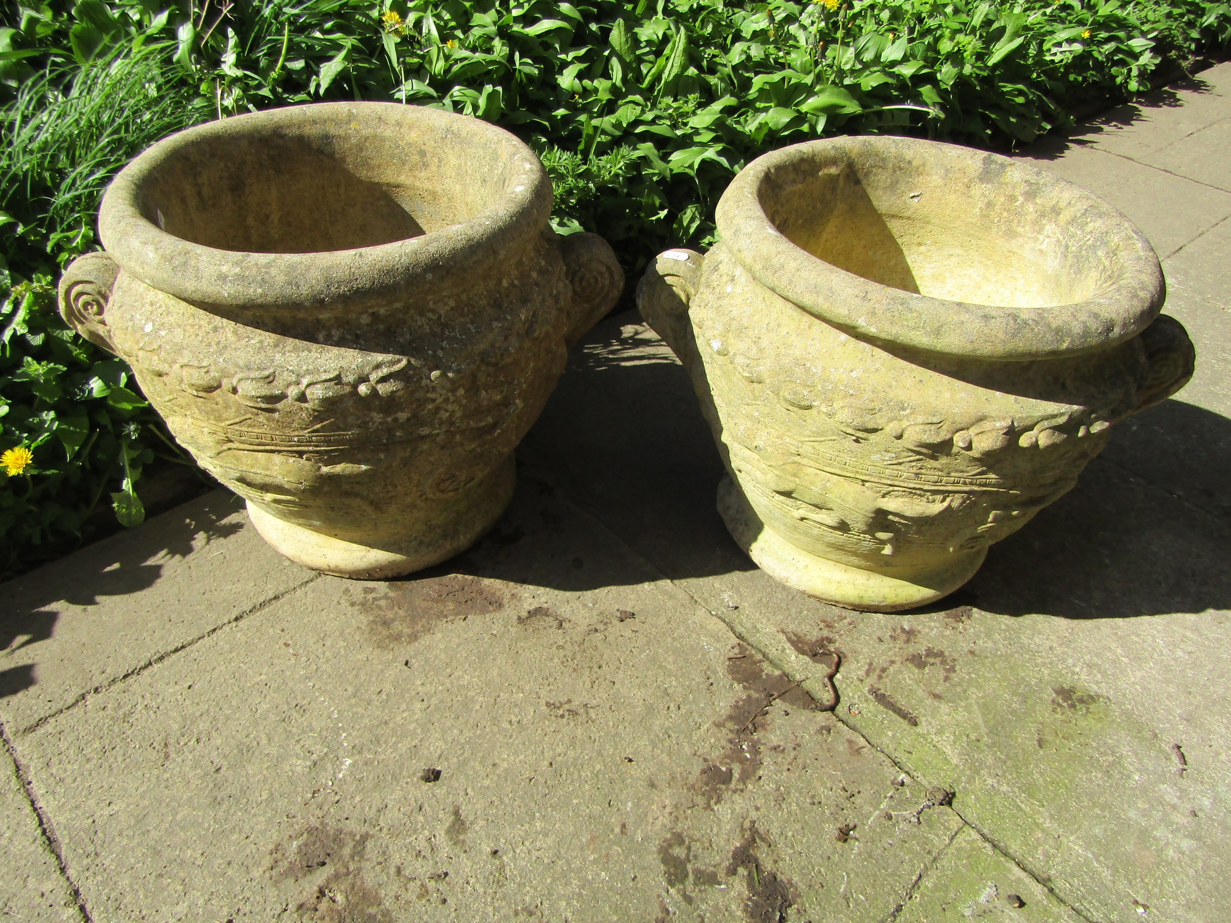 A pair of weathered cast composition stone roman type urns, the circular bowls with fixed scrolled