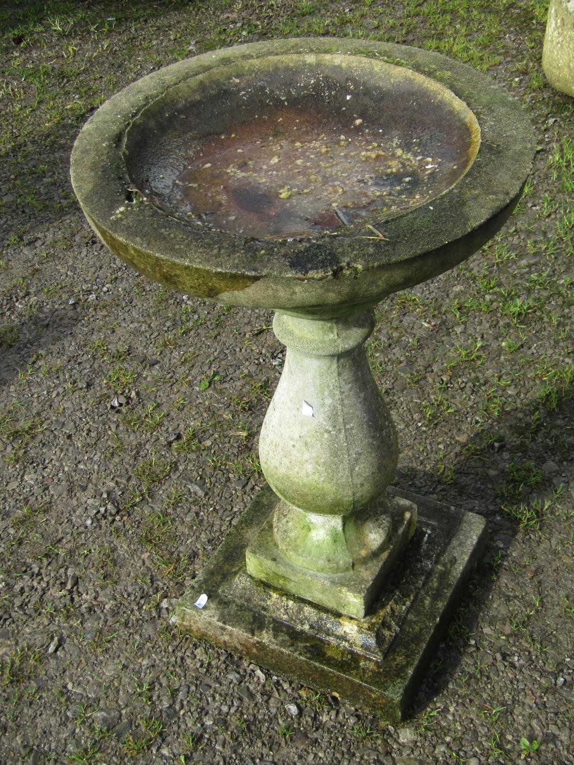 A weathered cast composition stone bird bath, raised on a baluster pedestal and square stepped base,