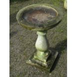 A weathered cast composition stone bird bath, raised on a baluster pedestal and square stepped base,