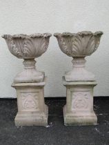 A pair of cast composition stone garden urns with circular acanthus leaf bowls raised on loose