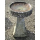 A weathered two sectional cast composition stone bird bath of circular form raised on a square