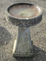 A weathered two sectional cast composition stone bird bath of circular form raised on a square