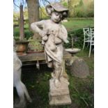 A weathered cast composition stone garden statue in the form of a boy wearing a brimmed hat
