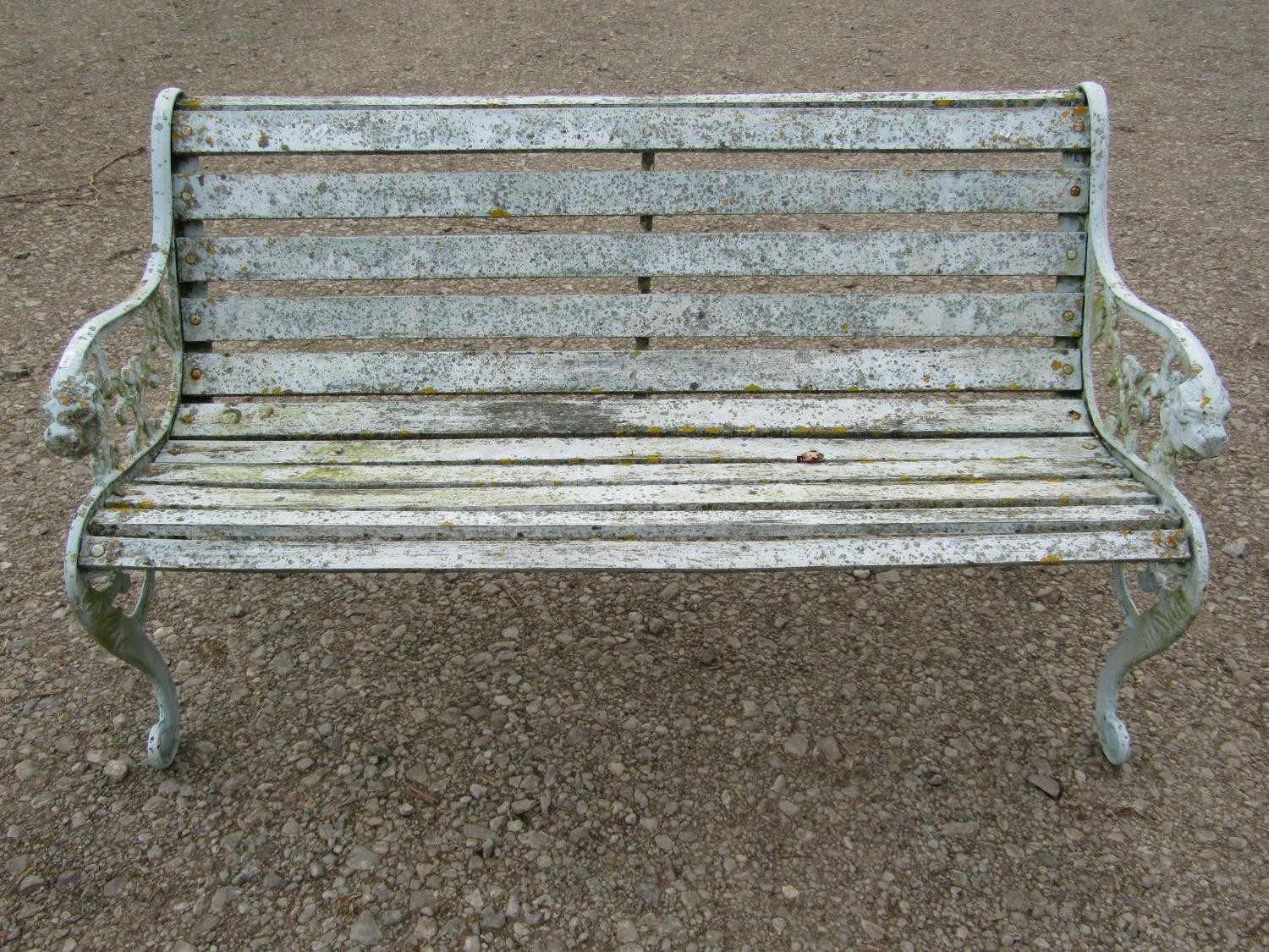 A weathered light blue/cream painted garden bench with slatted seat raised on decorative pierced and