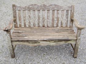 A Bridgman two seat weathered teak garden bench with slatted seat and back beneath a shaped rail