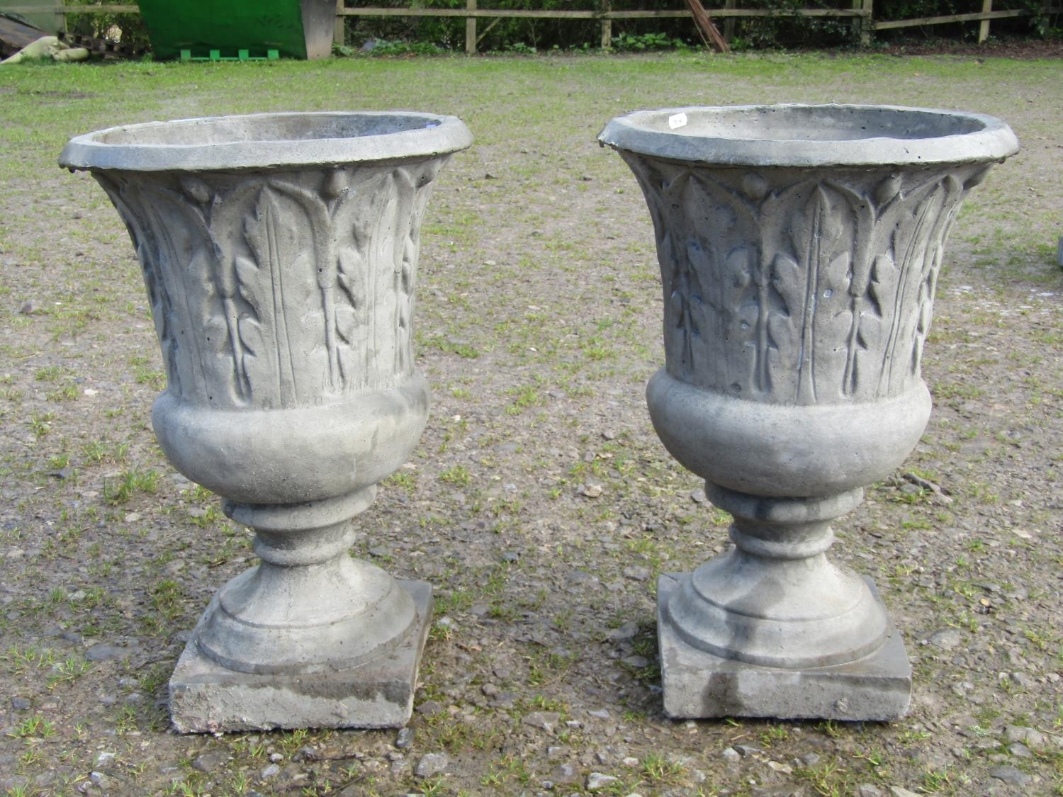 A pair of composition stone trumpet shaped garden urns, with moulded acanthus detail, raised on