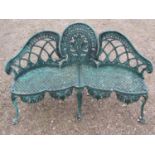 A weathered green painted cast alloy garden bench with shaped outline and decorative pierced