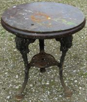 A weathered cast iron pub table with pierced and swept supports beneath a circular laminated