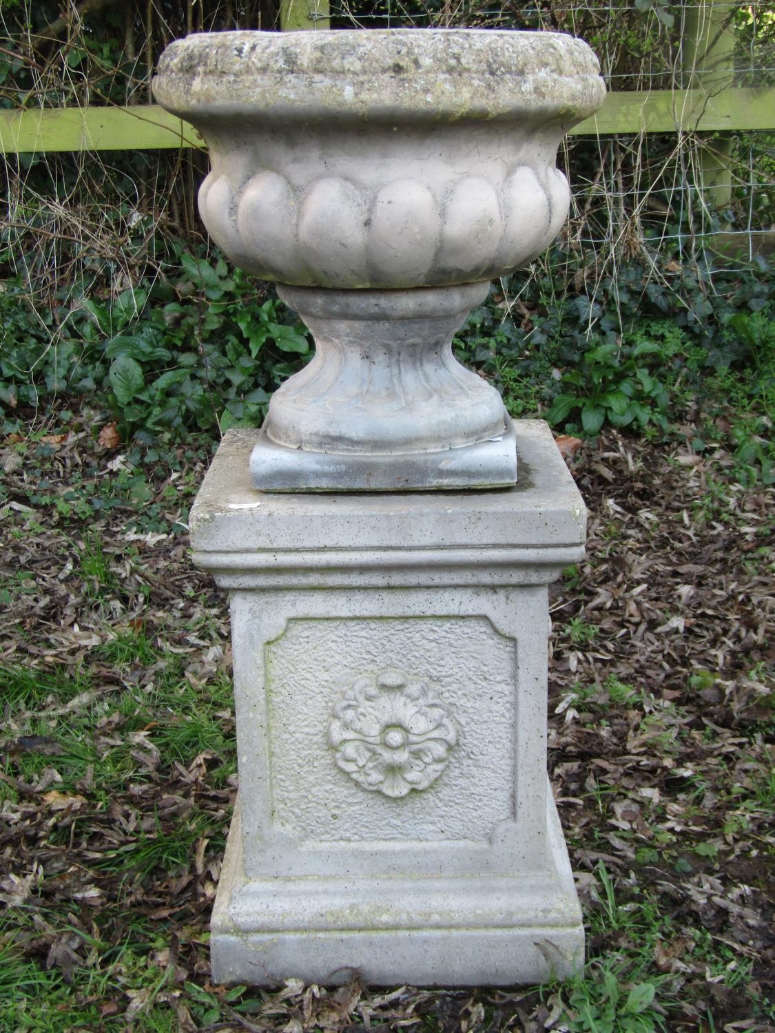 A weathered Sandford Stone cast garden urn with circular lobed bowl raised on a loose socle and