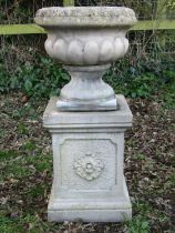 A weathered Sandford Stone cast garden urn with circular lobed bowl raised on a loose socle and