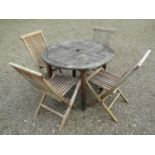 A small weathered teak garden table with circular slatted top, raised on square cut supports,