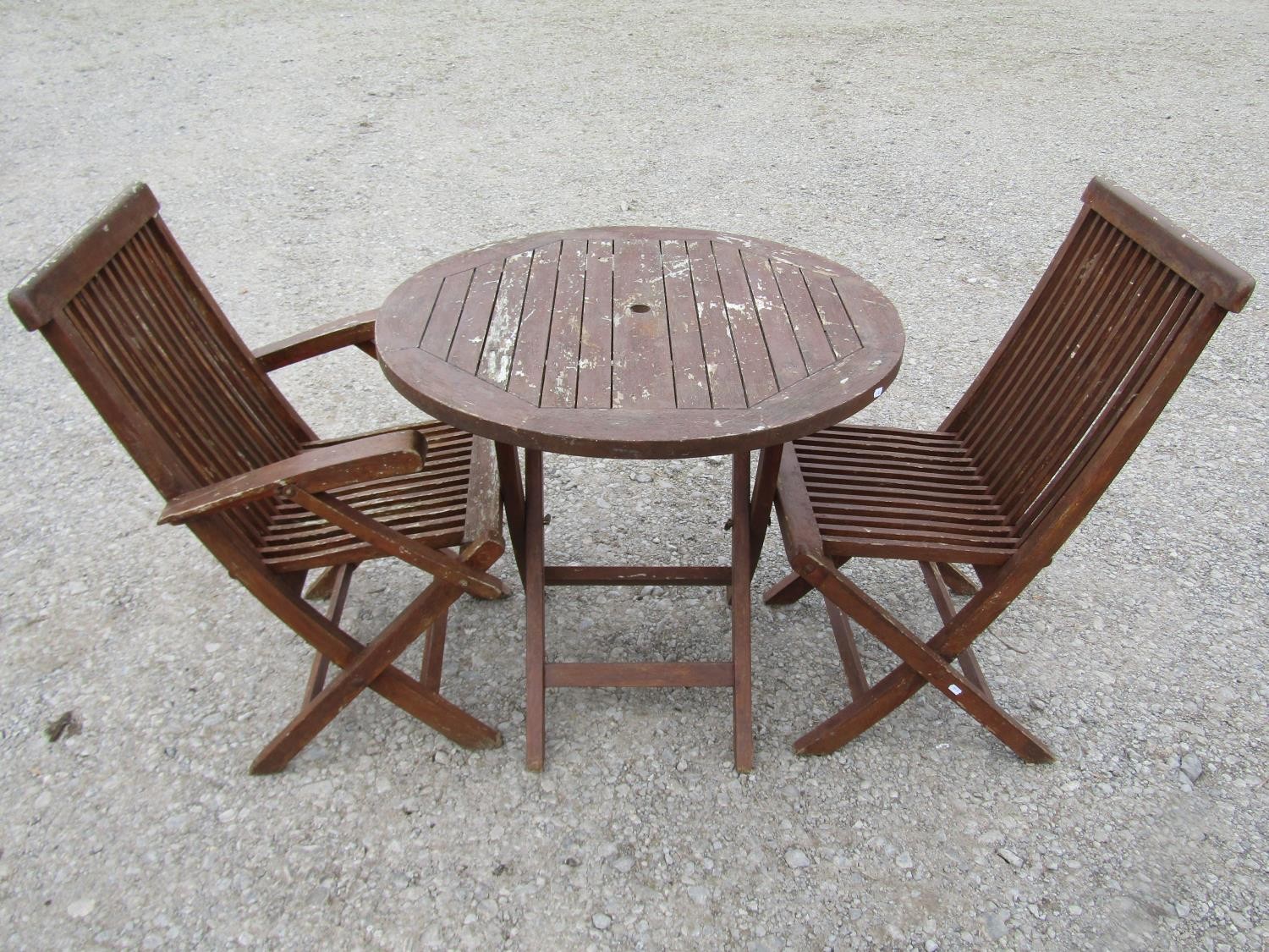 A weathered stained teak circular folding three piece garden terrace set comprising circular slatted