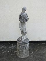 A weathered cast composition stone garden figure of a standing classical maiden carrying flowers,