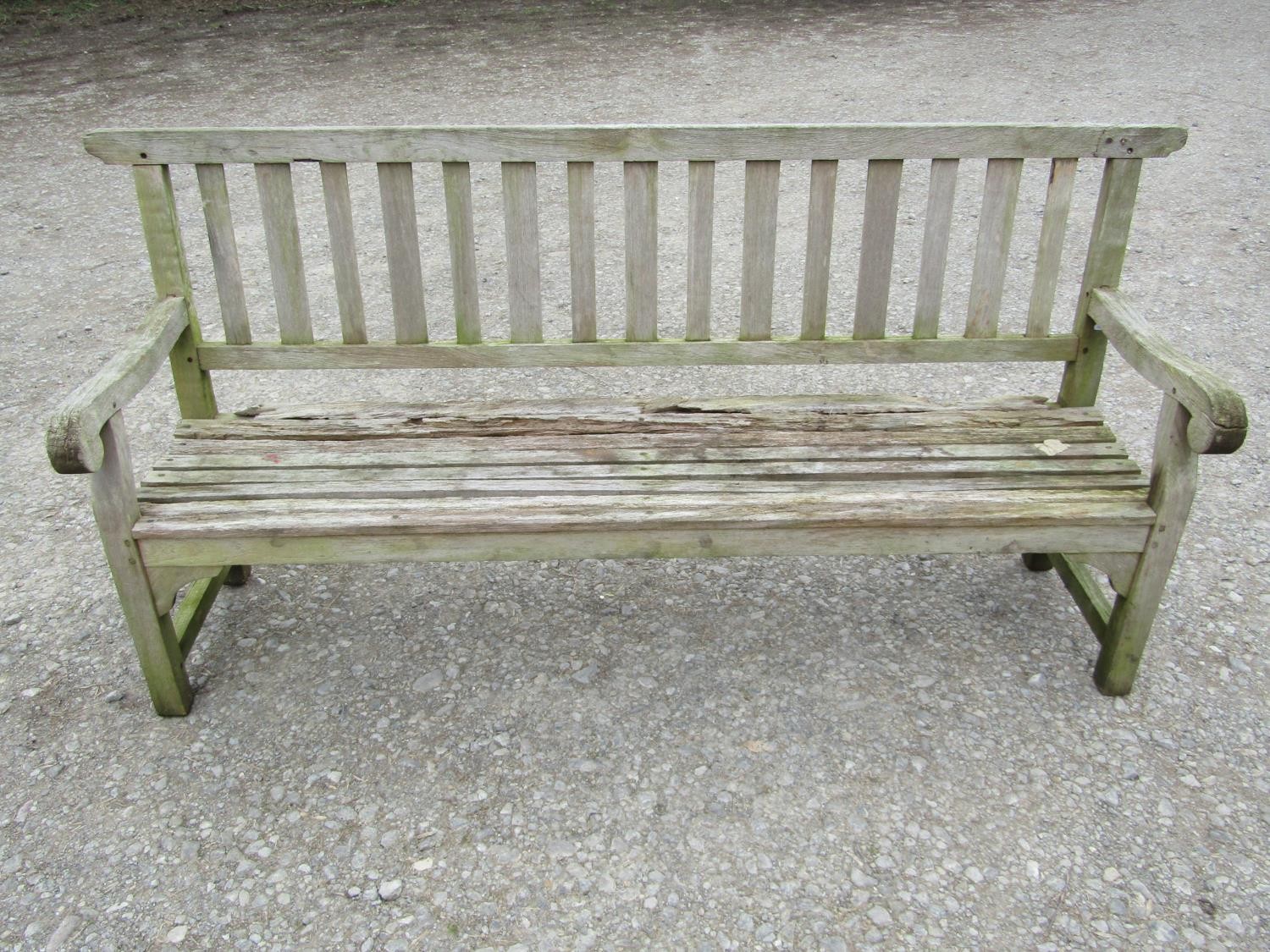 A well weathered teak garden bench with slatted seat and back and open scrolled arms, 198 cm long (