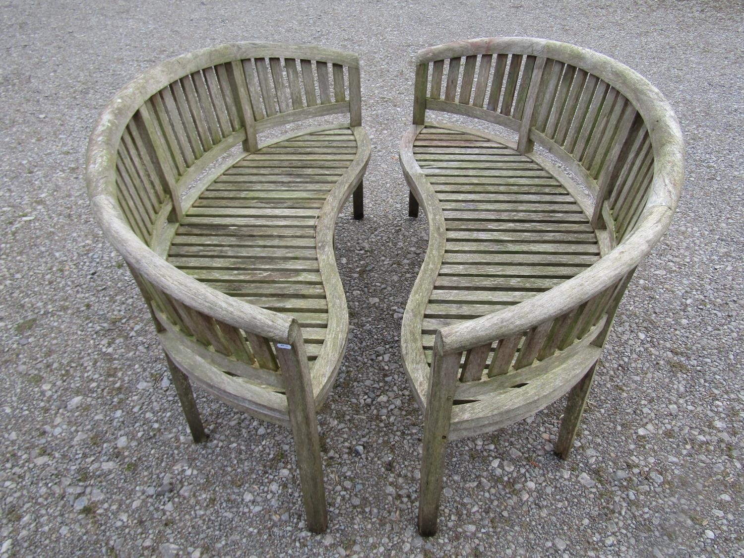 A pair of weathered teak banana shaped garden benches with loose seat cushions, 160 cm wide