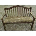 A weathered and stained teak garden bench with slatted seat and back beneath an arched rail, 120 cm,