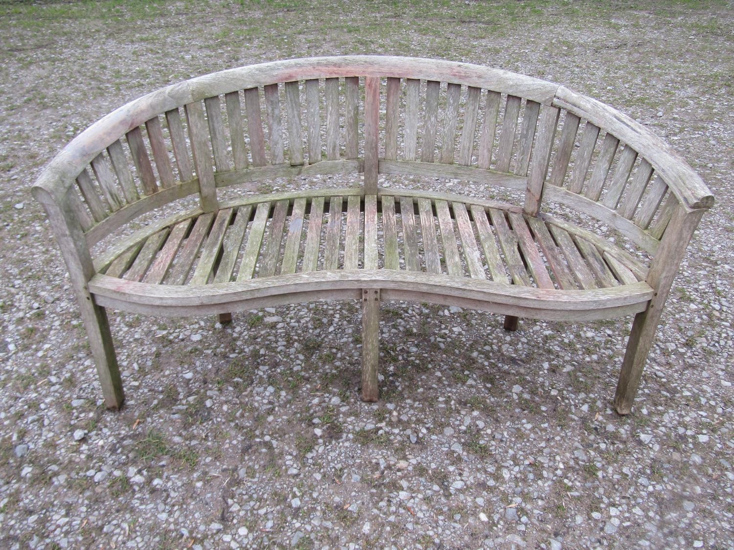 A weathered teak banana shaped garden bench, 156cm wide (af)