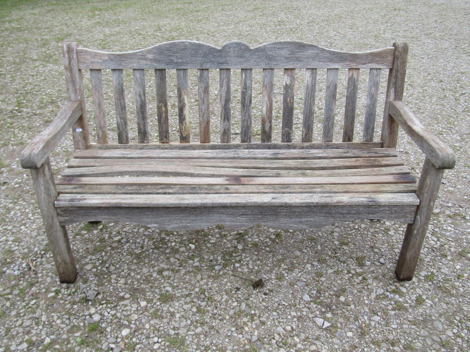 A Bridgman weathered teak three seat garden bench with slatted seat and back beneath a shaped rail
