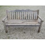 A Bridgman weathered teak three seat garden bench with slatted seat and back beneath a shaped rail