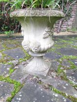 A weathered cast composition stone garden urn with flared egg and dart rim, lobed bowl with mask and