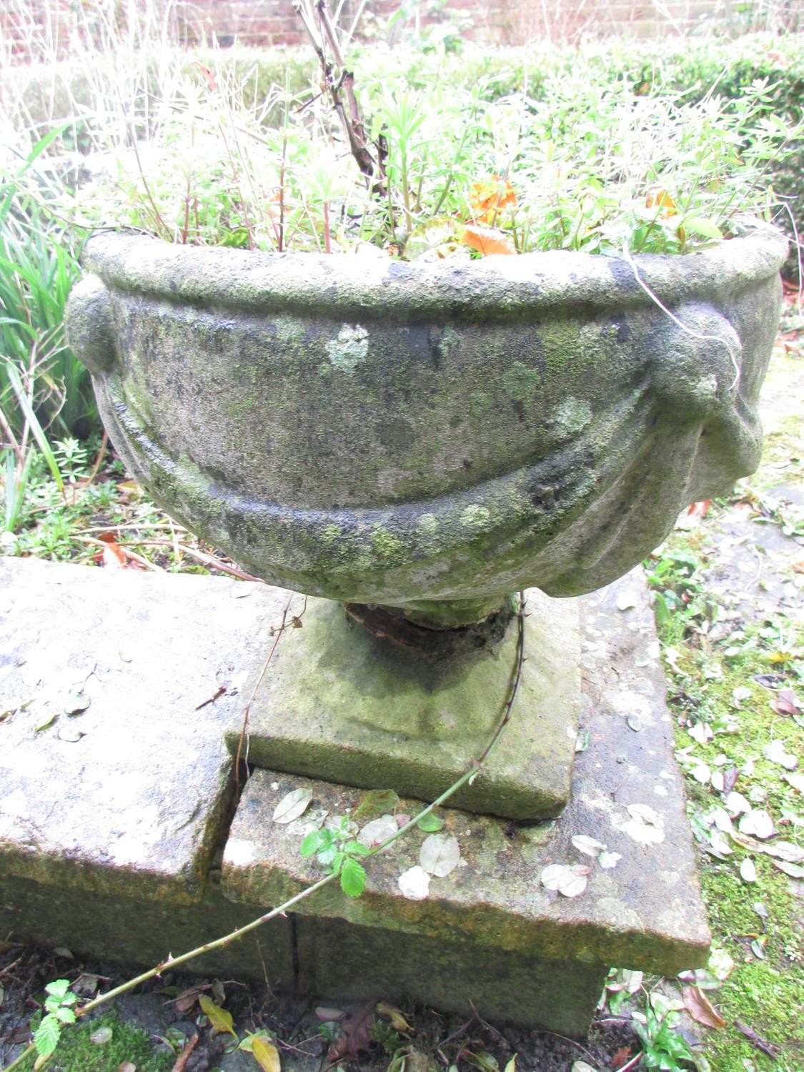 A pair of weathered cast composition stone garden urns, the circular bowls with classical swag