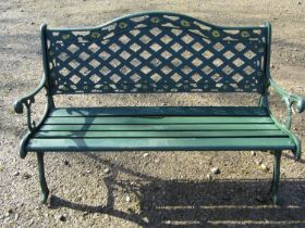 A green painted garden bench with wooden slatted seat beneath a cast iron pierced lattice panelled