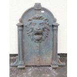 A cast iron fountain head the arched plate with lions mask detail flanked by reeded columns and C