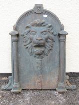 A cast iron fountain head the arched plate with lions mask detail flanked by reeded columns and C