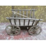 An antique wooden hand cart with open slatted sides and four spoke wheels with iron rims