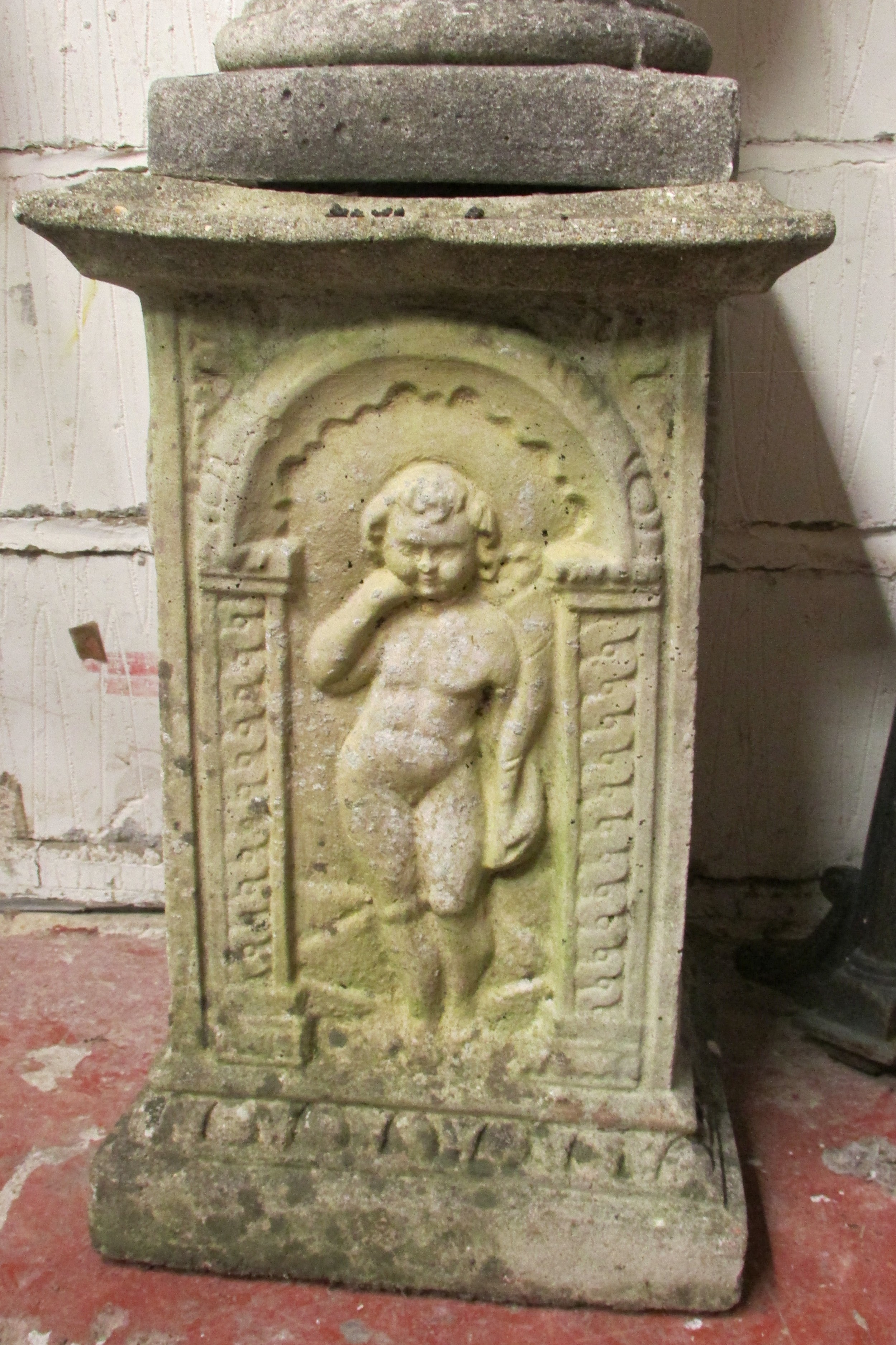 A weathered cast composition stone cherub astride a sphere clutching a floral garland raised on a - Image 3 of 3
