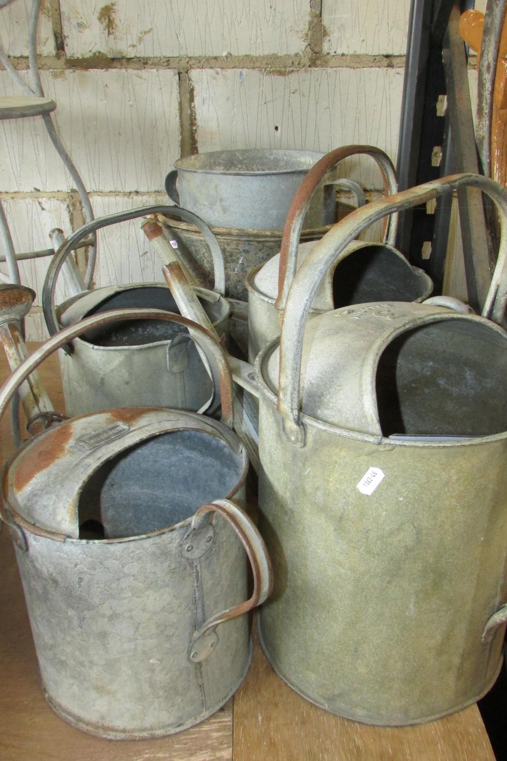 Five vintage galvanised watering cans of varying design and capacity together with a bucket and a