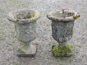 A pair of weathered cast composition stone urns with flared rims and lobed bodies, and mythical