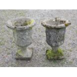 A pair of weathered cast composition stone urns with flared rims and lobed bodies, and mythical