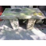 A weathered rough hewn stone garden bench with rectangular slab seat, raised on square cut supports,