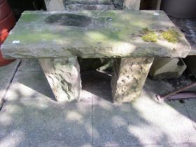 A weathered rough hewn stone garden bench with rectangular slab seat, raised on square cut supports,