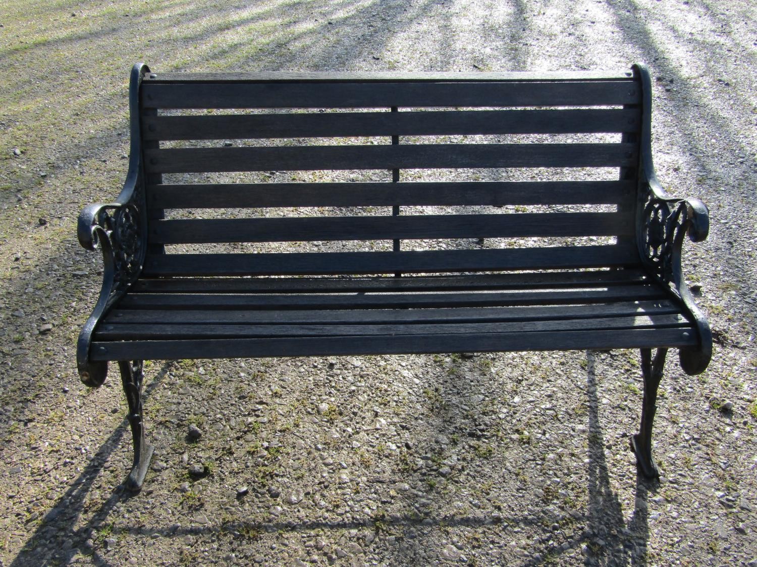 A two seat garden bench with stained wooden slatted seat raised on decorative pierced and scrolled
