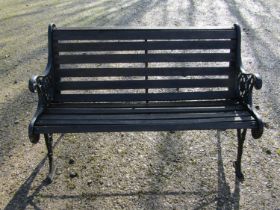 A two seat garden bench with stained wooden slatted seat raised on decorative pierced and scrolled