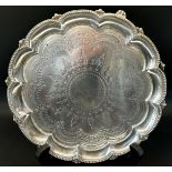 A Victorian silver card tray with scalloped edge and floral engravings, raised on scrolled feet,
