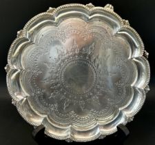 A Victorian silver card tray with scalloped edge and floral engravings, raised on scrolled feet,